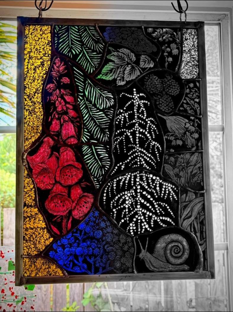 The Under-land Gardenscape panel hanging in a window: foxglove, ferns and a snail painted on dark glass